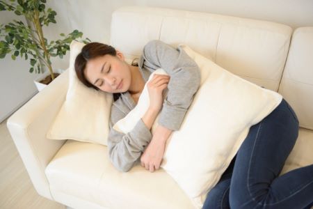 抱き枕を抱いてソファで寝る女性の画像